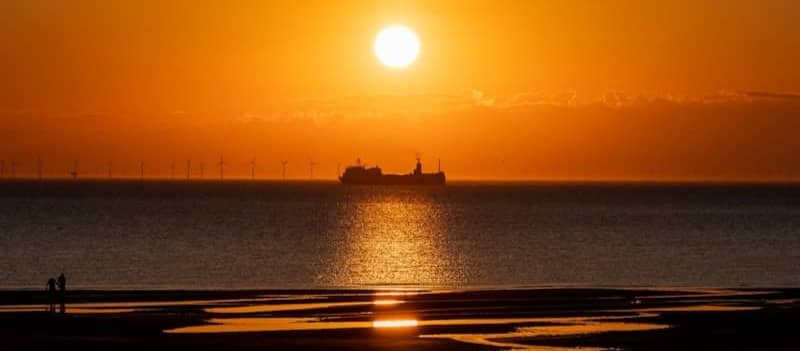 Sunset shines over the ocean with a ship.