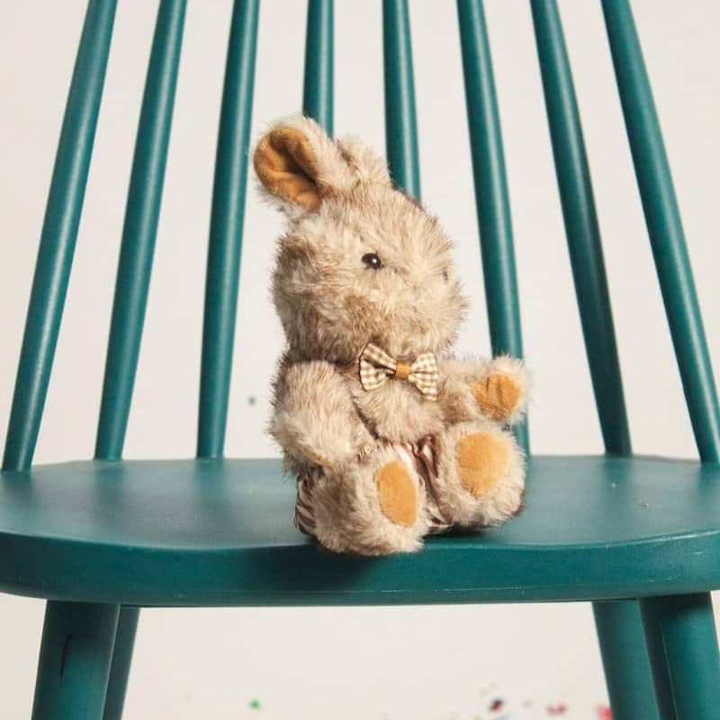 A plush toy rabbit wearing a bow tie on a teal wooden chair