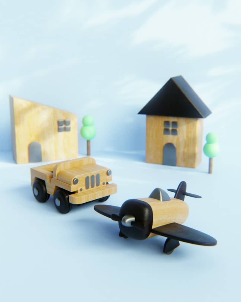 Wooden toy car and airplane with small houses and trees on blue background