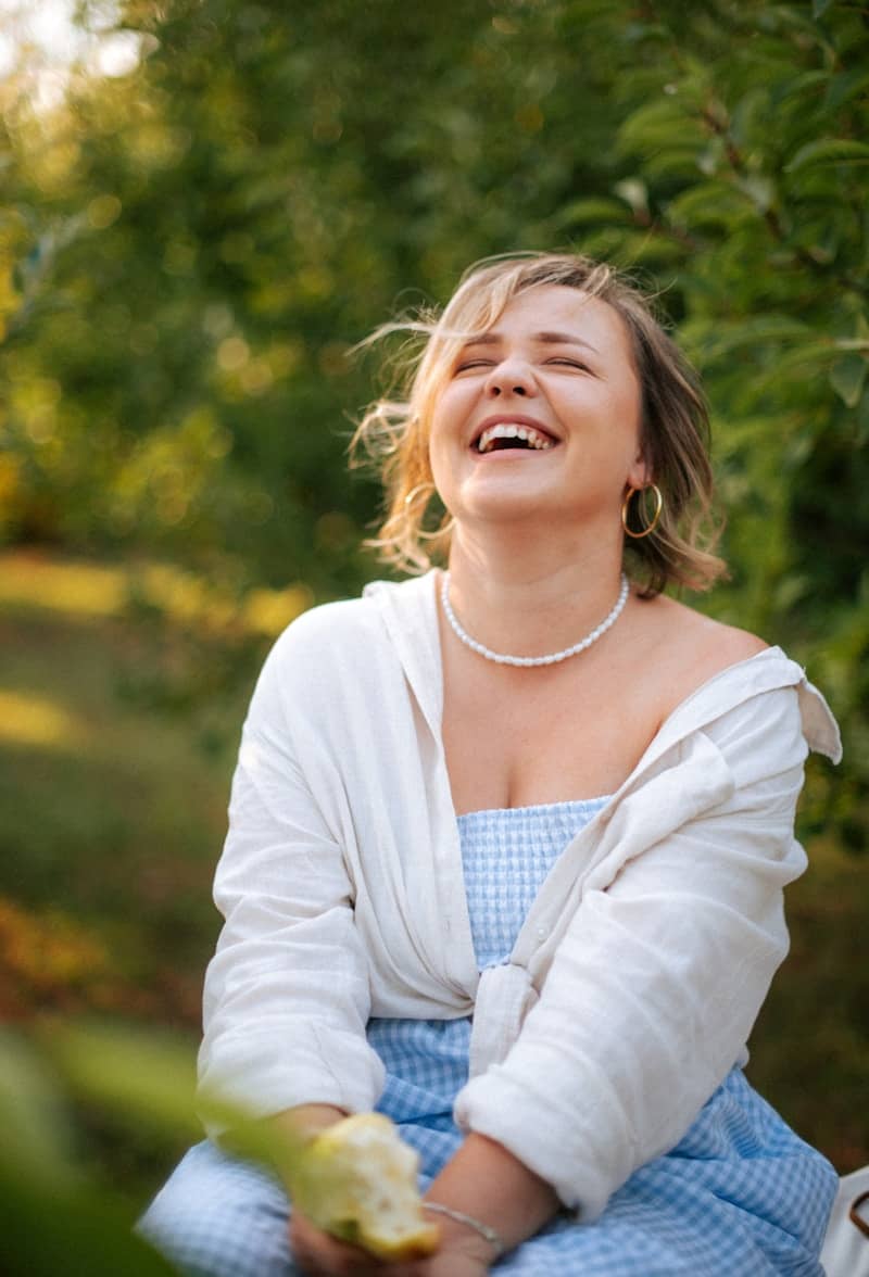 A woman laughing outdoors in a park.