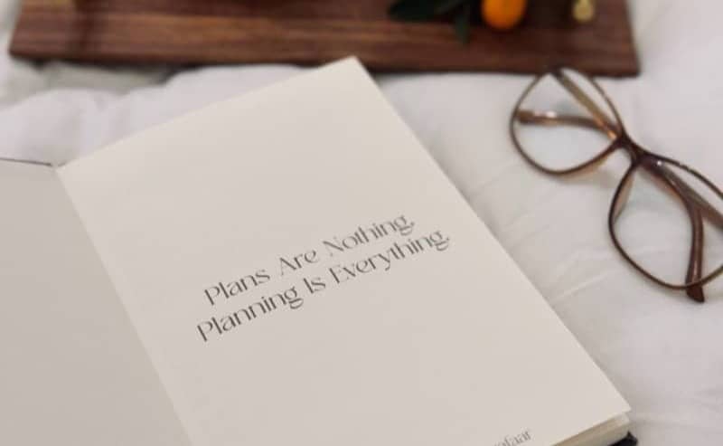 An open book sitting on top of a bed next to a bowl of fruit