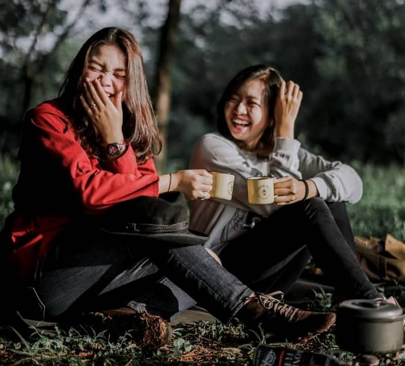 two women holding cups laughing at each other