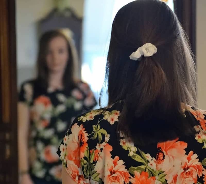 woman wearing black and multicolored blouse and blue denim jeans facing mirror inside white concrete room