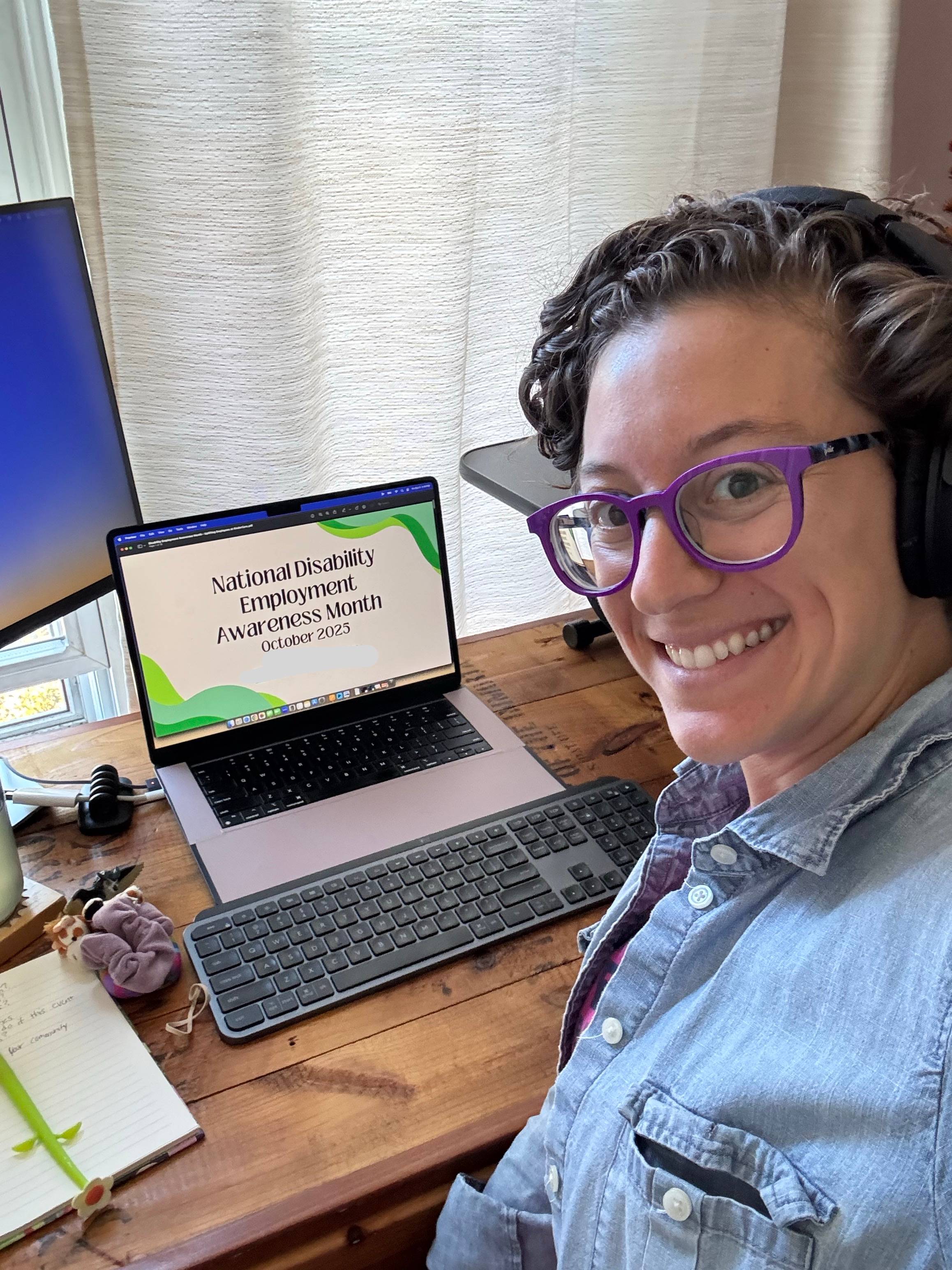 Lauren smiling, taking a selfie over her shoulder, in front of her laptop, with a presentation cover slide on the screen that reads "National Disability Employment Awareness Month - October 2025"