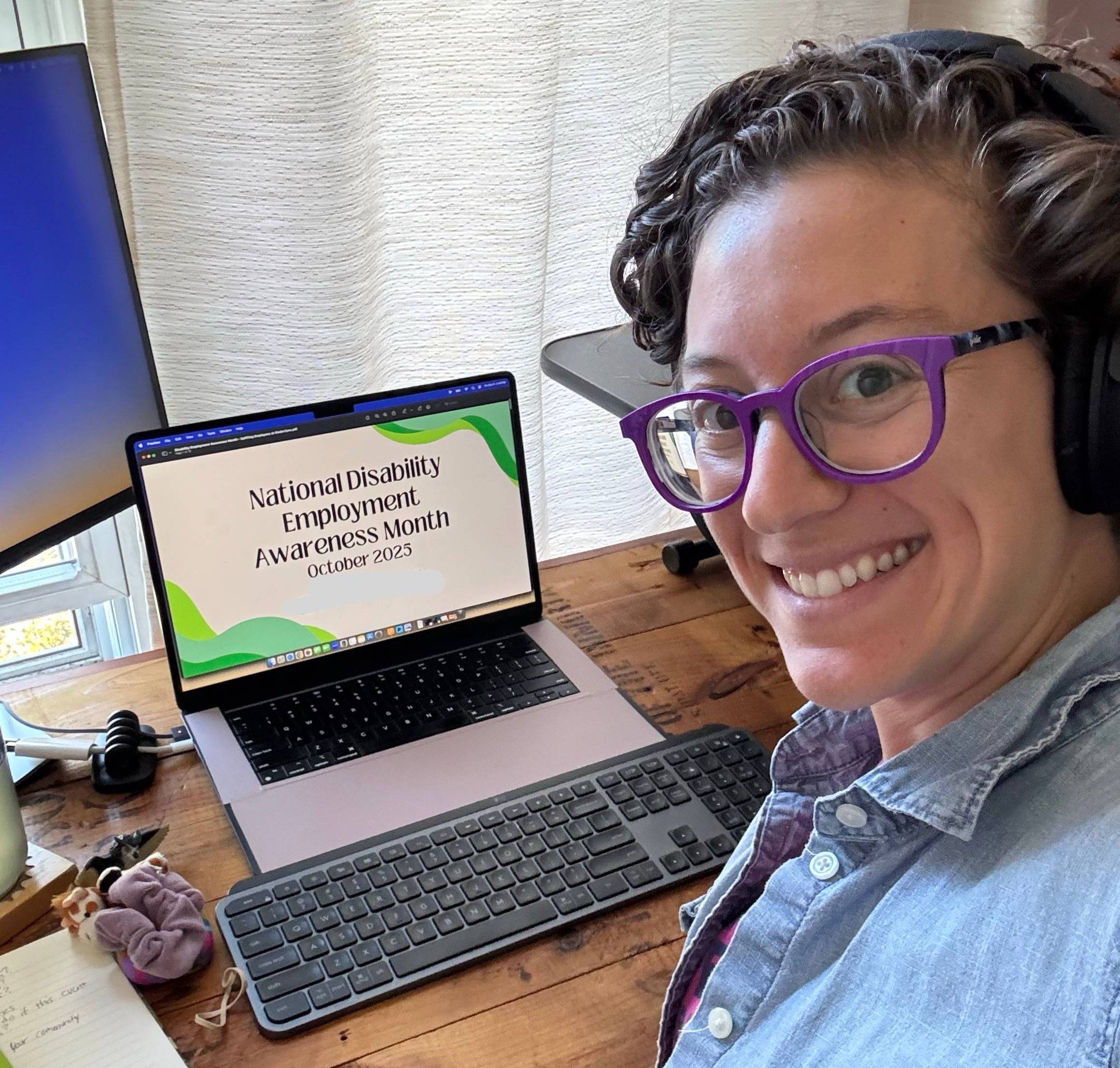 Lauren smiling, taking a selfie over her shoulder, in front of her laptop, with a presentation cover slide on the screen that reads "National Disability Employment Awareness Month - October 2025"