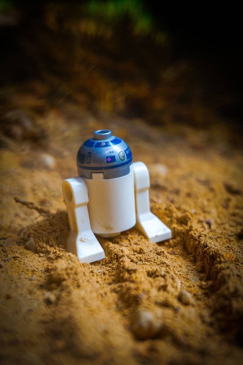 A lego r2-d2 figure rests in sand.