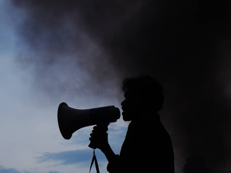 A silhouette of a woman holding a megaphone in front of a cloud of smoke