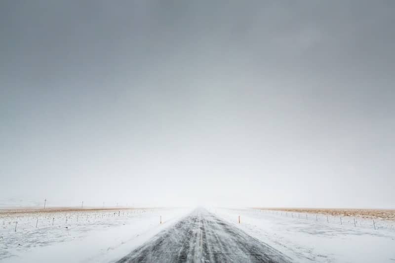 Snowy road disappears into a hazy, overcast sky.