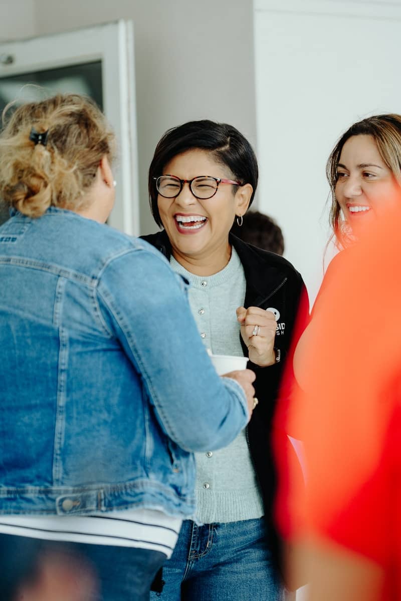 Three women laughing together in a bright indoor space