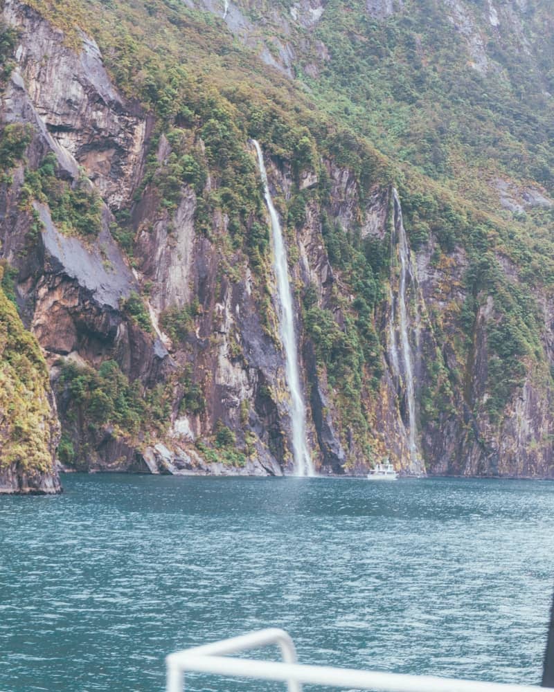 Waterfalls cascade down a steep, rocky mountainside into the ocean.