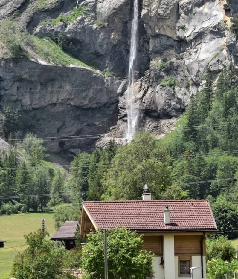 Tall waterfall cascades down a rocky cliff above a village.
