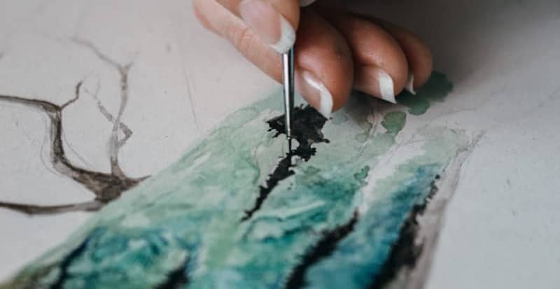 A hand paints watercolor art with a fine brush.