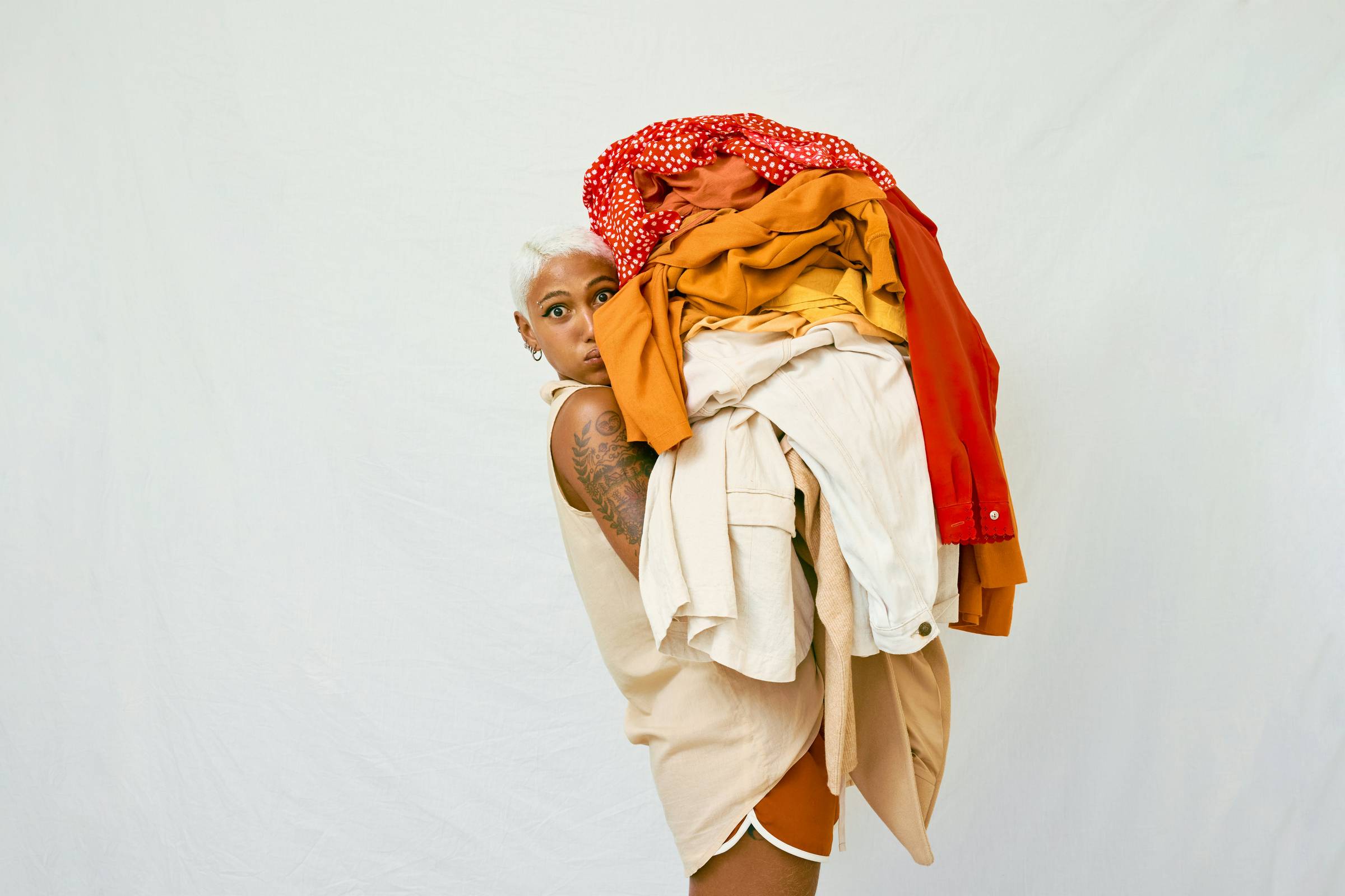 A person with short, light gray hair peeks out from behind a large, colorful pile of folded laundry.