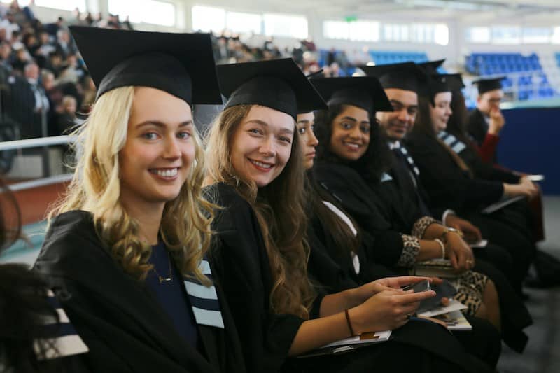 A row of graduates in black caps and gowns sitting at a ceremony