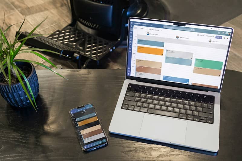 A laptop and a smartphone displaying a scheduling calendar on a black desk
