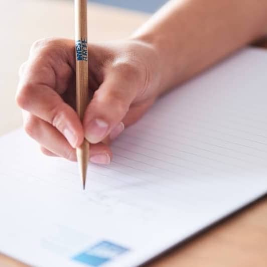 A hand holds a pencil, writing on a lined paper.
