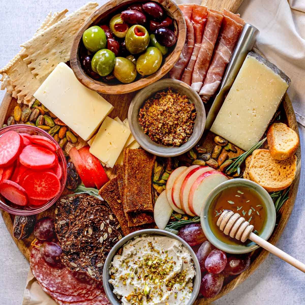 Round charcuterie board with meat, cheese, crackers, fruit, and veggies.