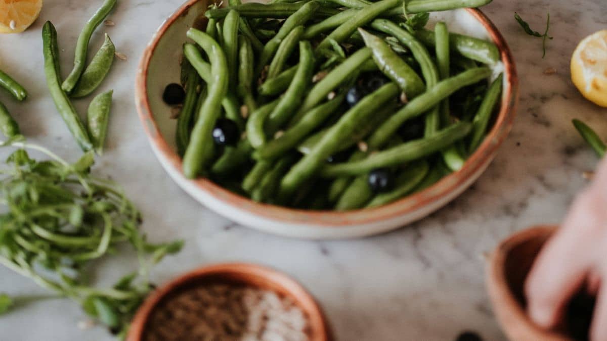 Ceramic bowl of green beans with seeds and blueberries.