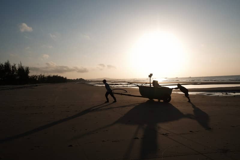 Two people pull a boat on a beach at sunset.