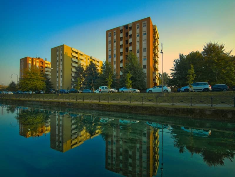 Apartment buildings reflected in a calm canal at sunset.