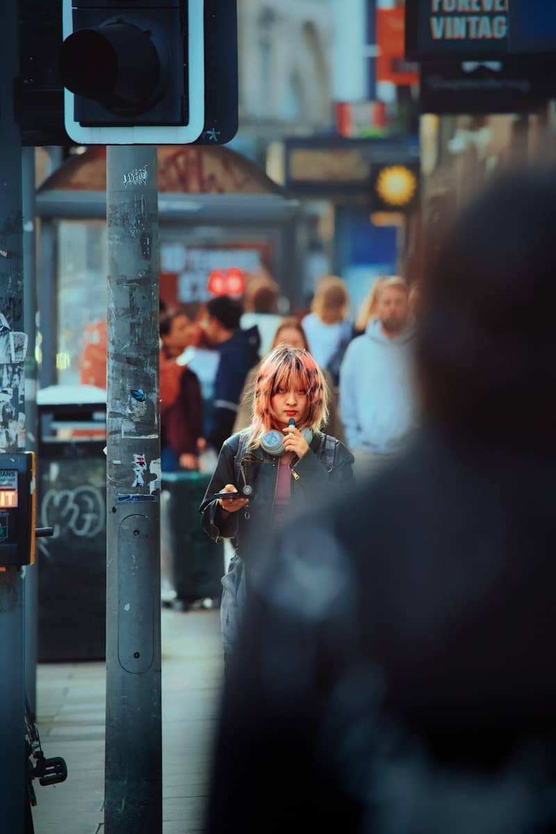 Pink-haired youth holding microphone and phone on a busy street