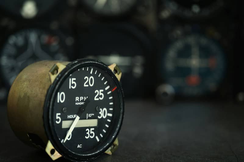 A vintage aircraft tachometer gauge with a black dial and white markings