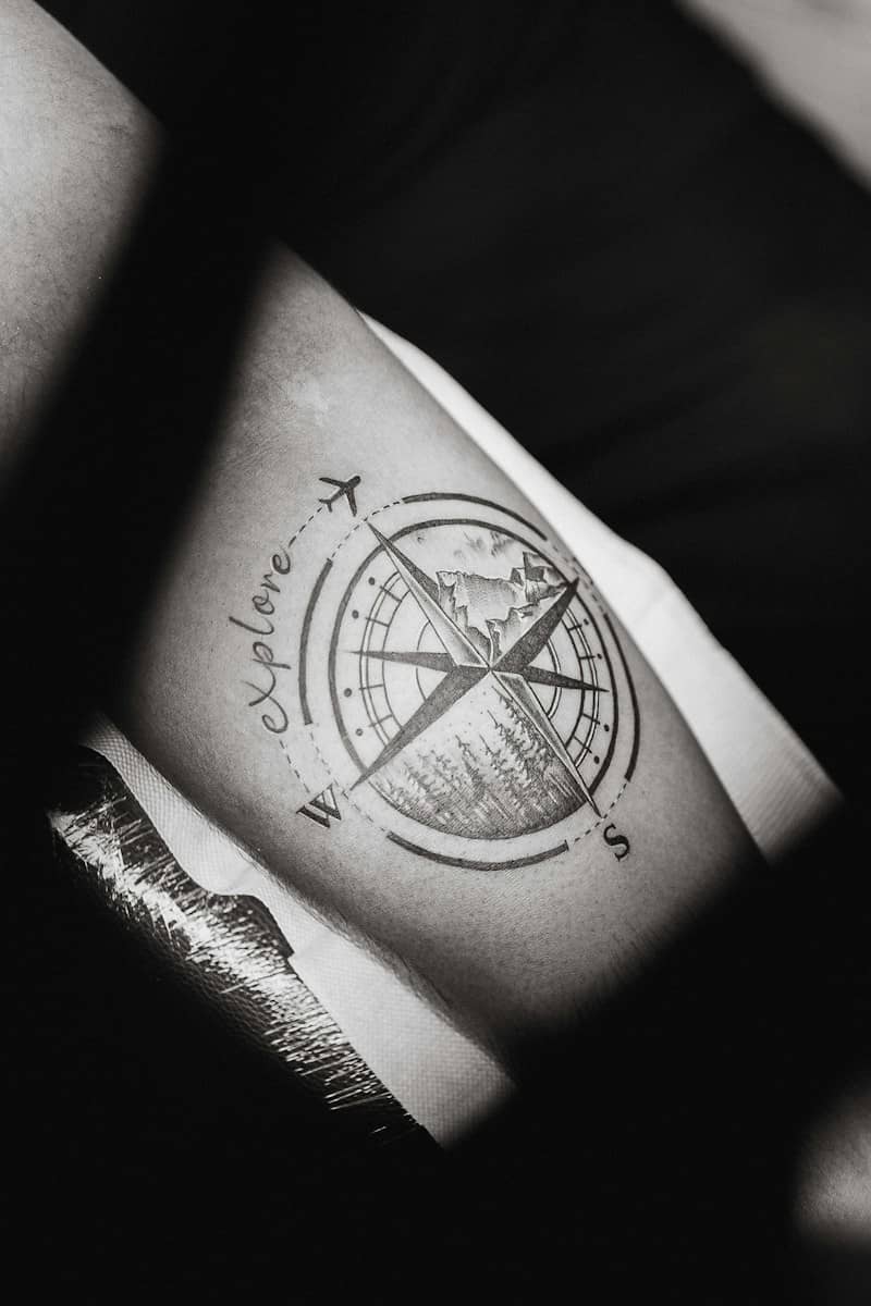 A compass tattoo with a mountain and forest design on a person's arm