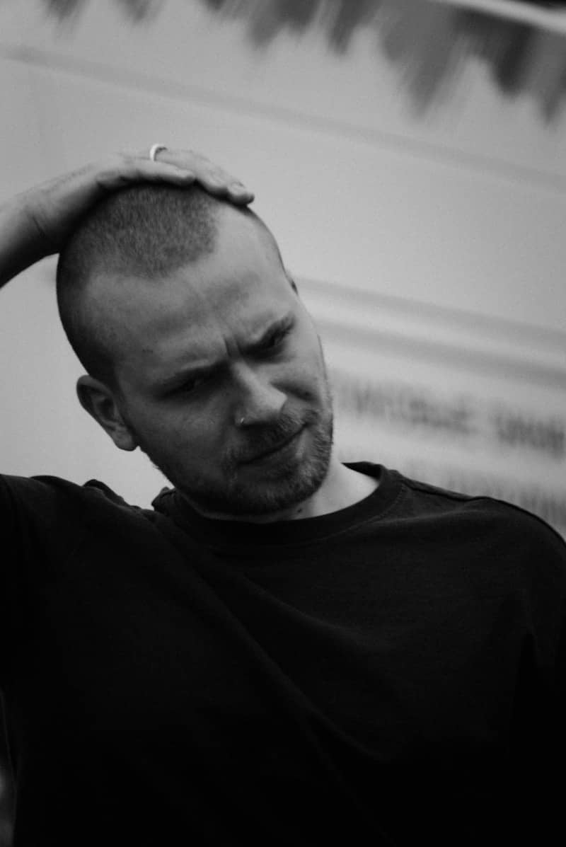 Bearded man with hand on head looking down.