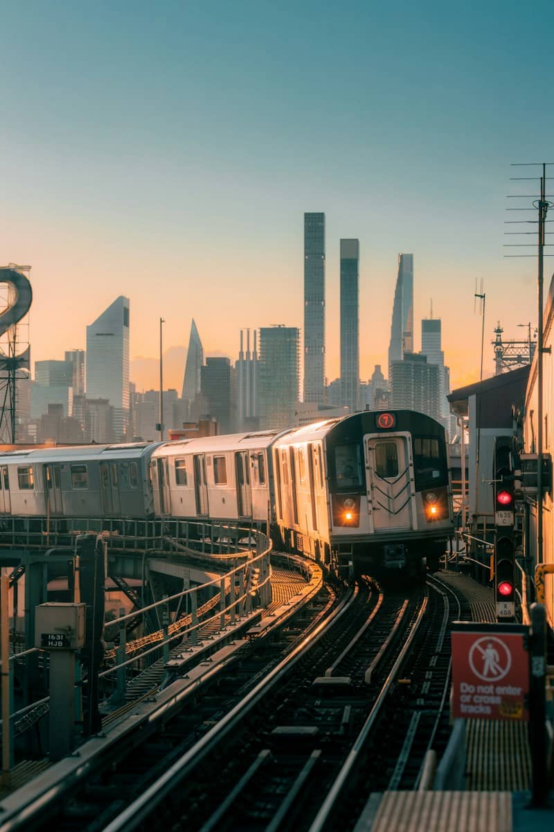 A 7 train on elevated tracks with the New York City skyline at golden hour