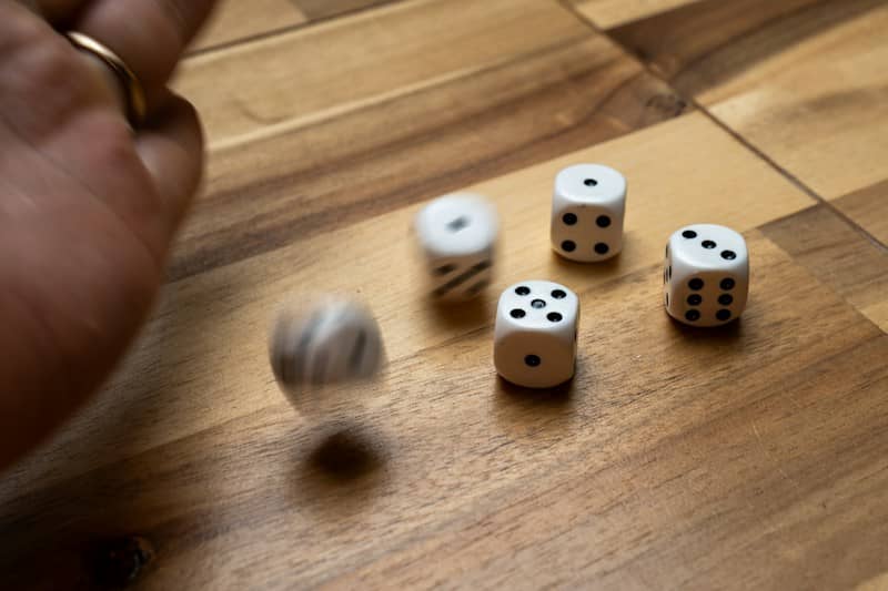 A hand rolling white dice across a wooden table with some dice in motion