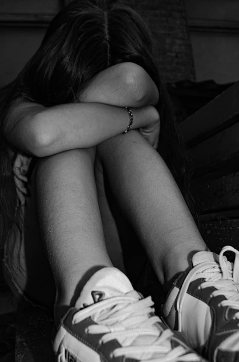 A person sitting, covering their face with their arms