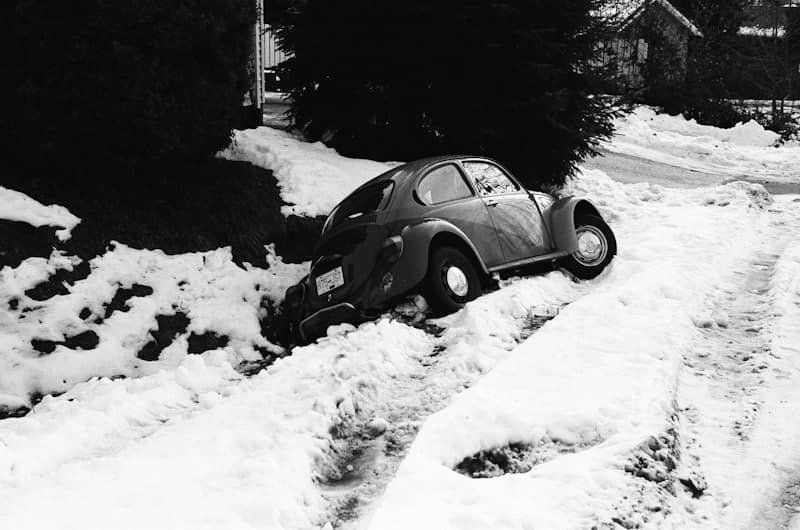 A Volkswagen Beetle stuck in a snow-covered ditch beside a road