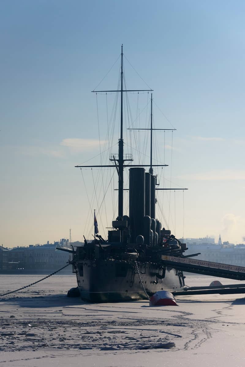 Silhouetted battleship docked in frozen water under a clear sky.