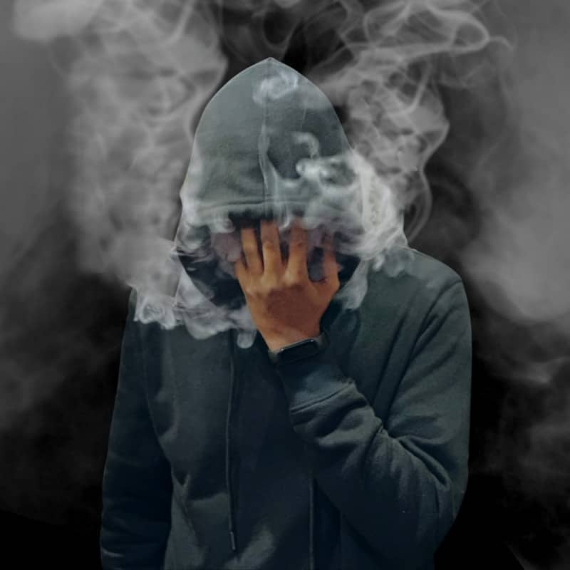 A man in a hoodie covers his face with smoke