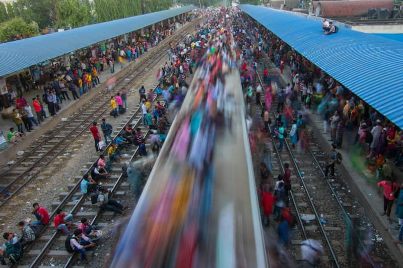 A motion-blurred train passing through a crowded railway station with people waiting on platforms