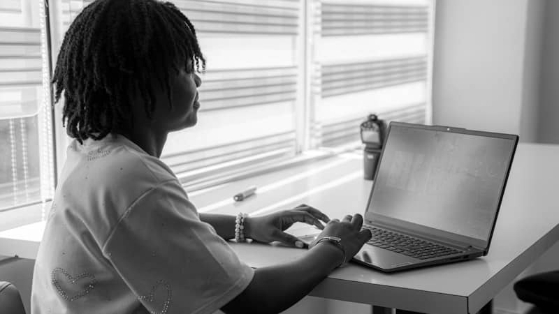 A person with dreadlocks typing on a laptop at a desk in a workspace