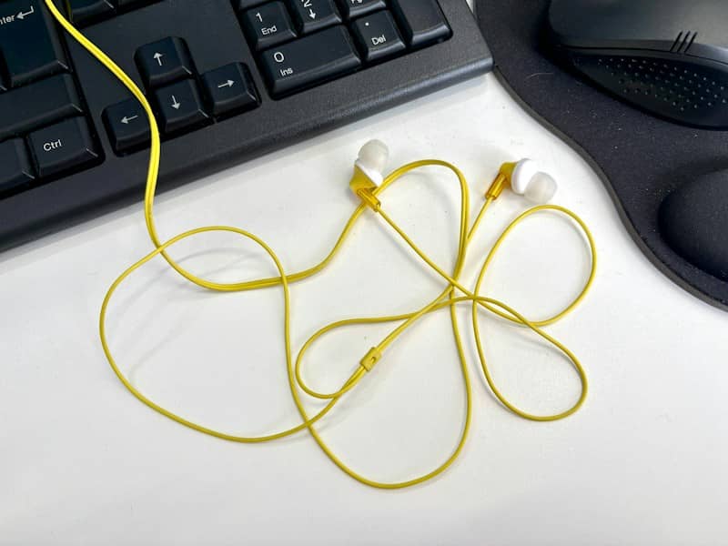 Yellow wired earbuds on a white desk beside a black computer keyboard