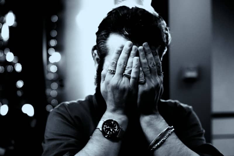 A person covers their face with hands, wearing a watch