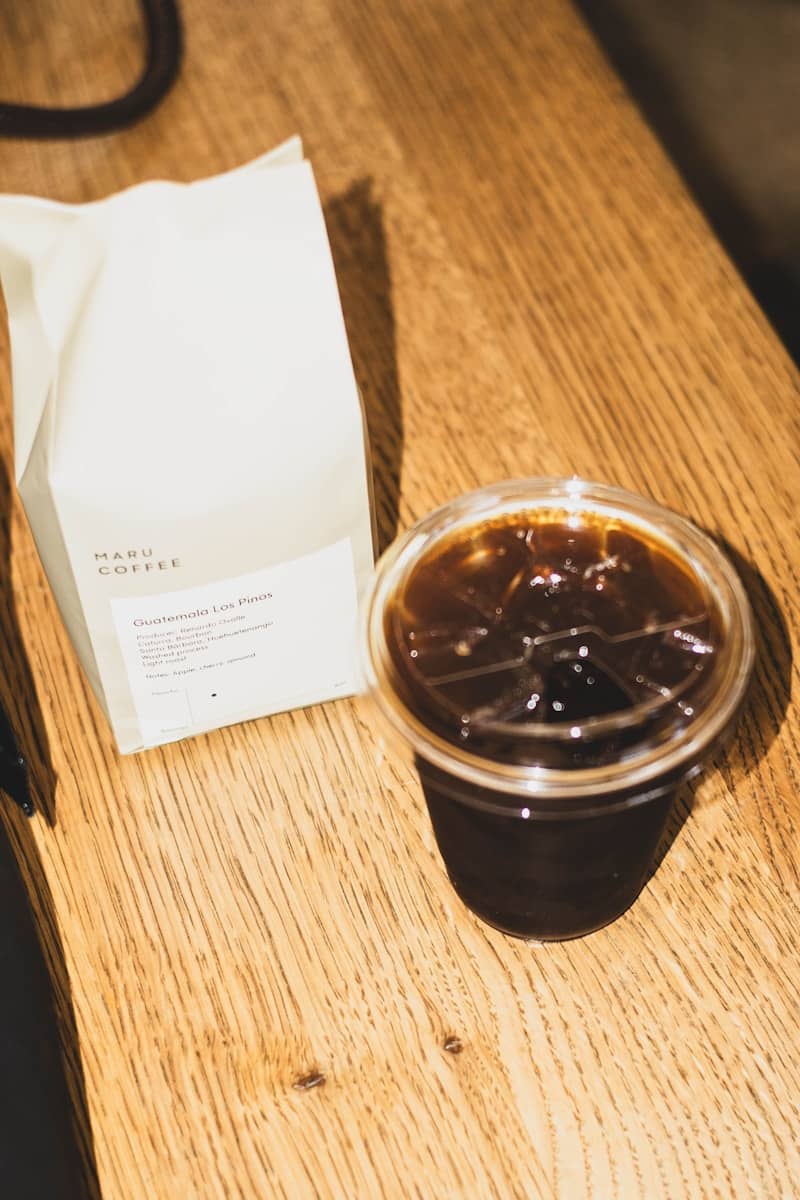 Iced coffee and bag of coffee beans on wooden table.