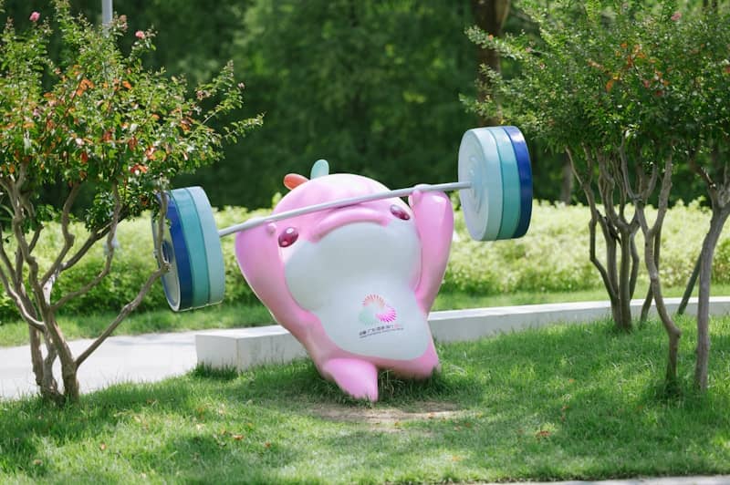 A pink cartoon mascot lifting a barbell in a green park