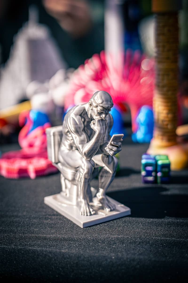 Silver thinker statue on toilet using smartphone