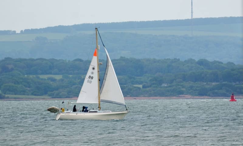 White sailboat with two people sailing on the water.