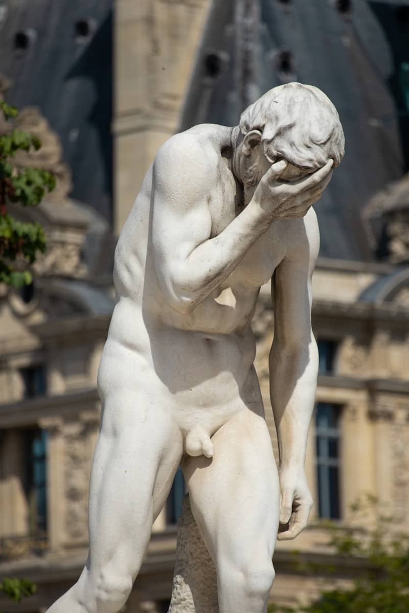A white marble statue of a man covering his face.