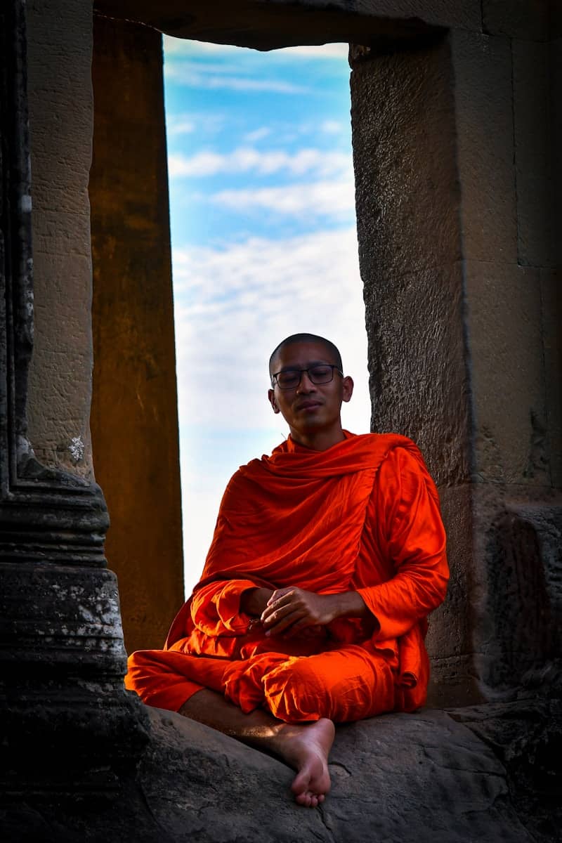 A buddhist monk in orange robes sits in a doorway.