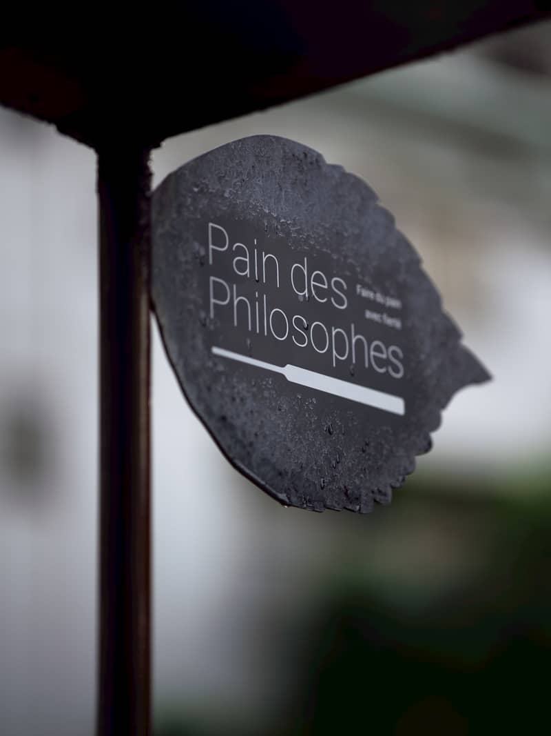 Dark leaf-shaped sign displaying "pain des philosophes" and a knife.
