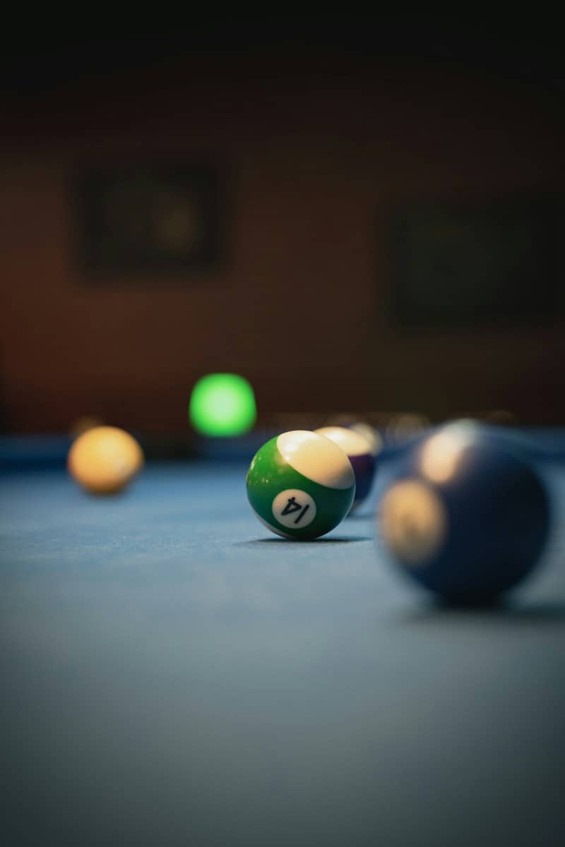A green fourteen billiard ball on a blue felt table with blurred balls
