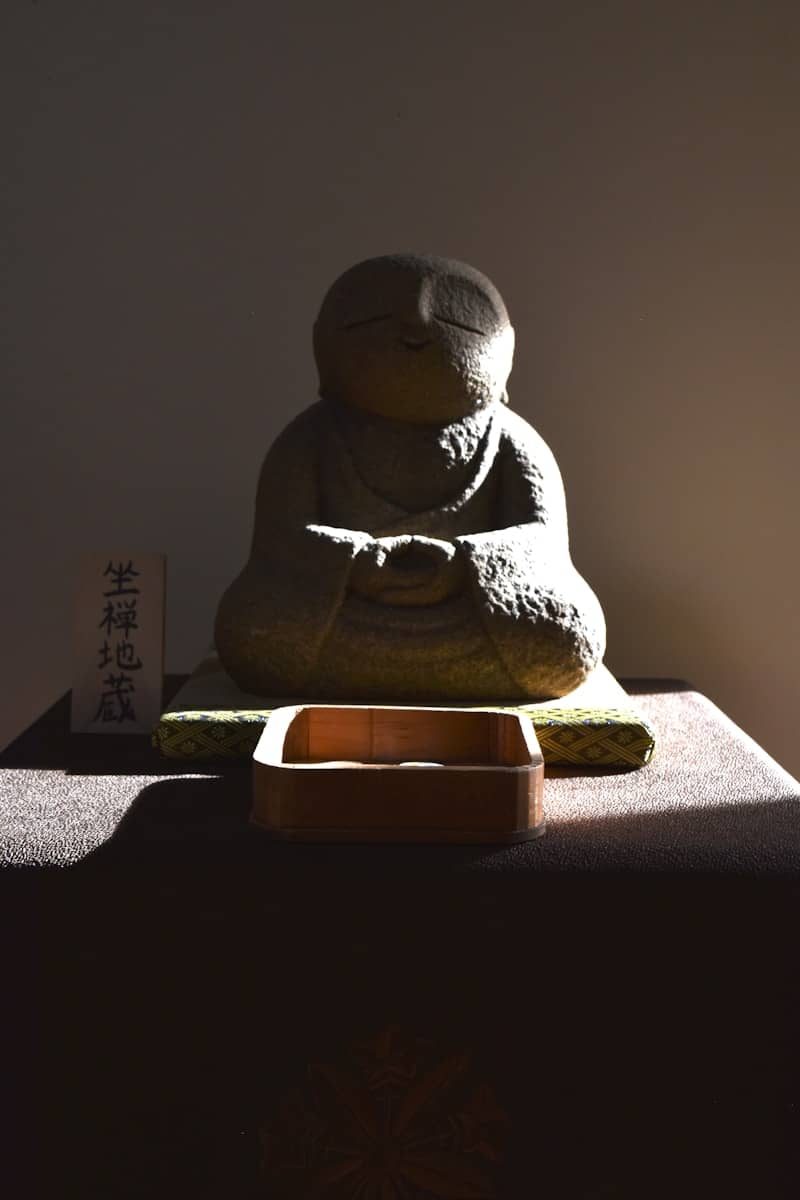 Stone statue of meditating monk with wooden offering bowl