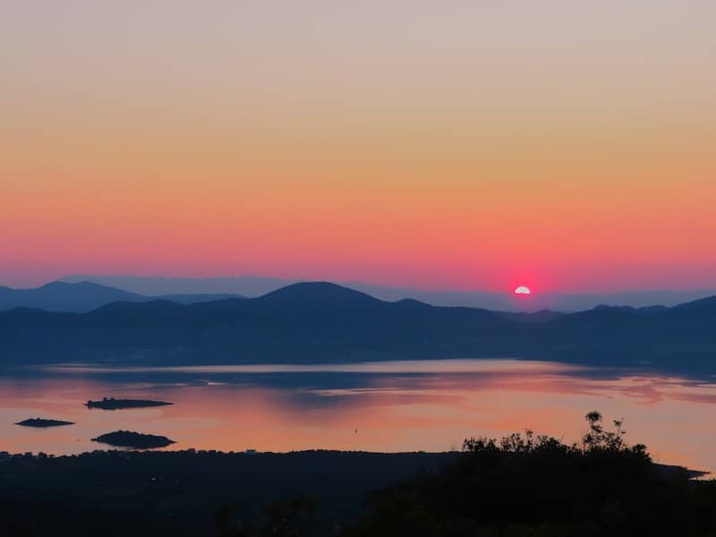 The sun is setting over a lake with mountains in the background