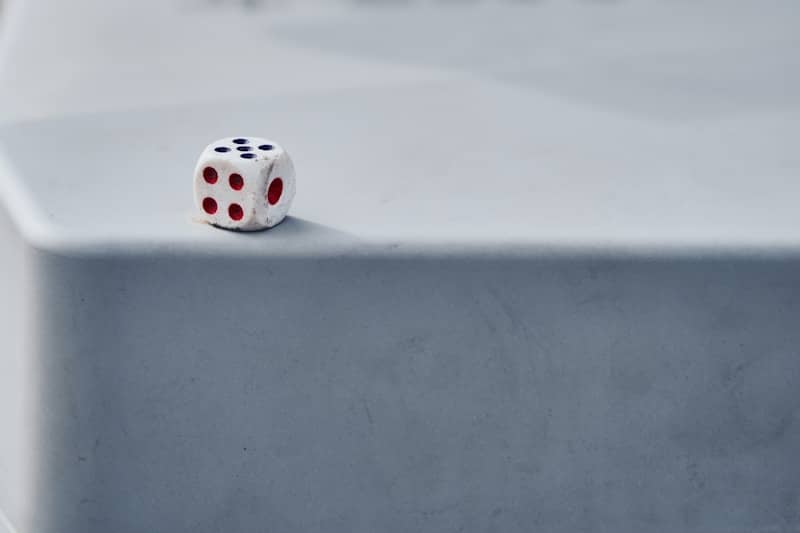A single white die rests on a gray surface.