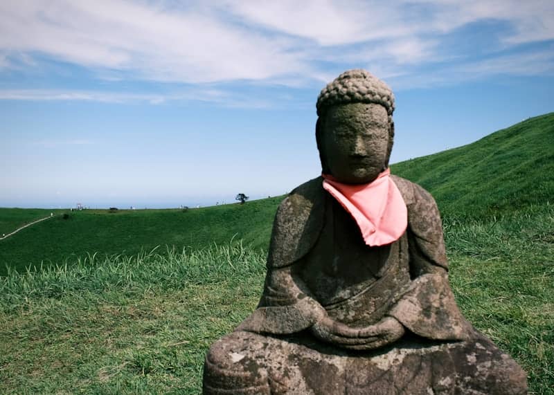 Stone buddha statue with pink scarf on a green hill.